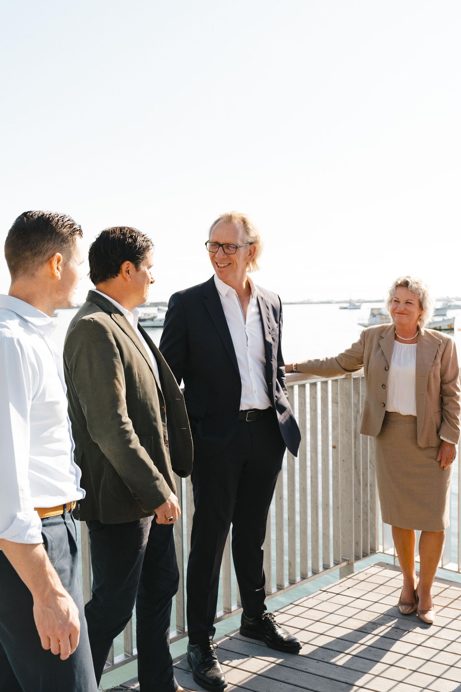 Business professionals having a casual discussion on an outdoor deck overlooking a waterfront.