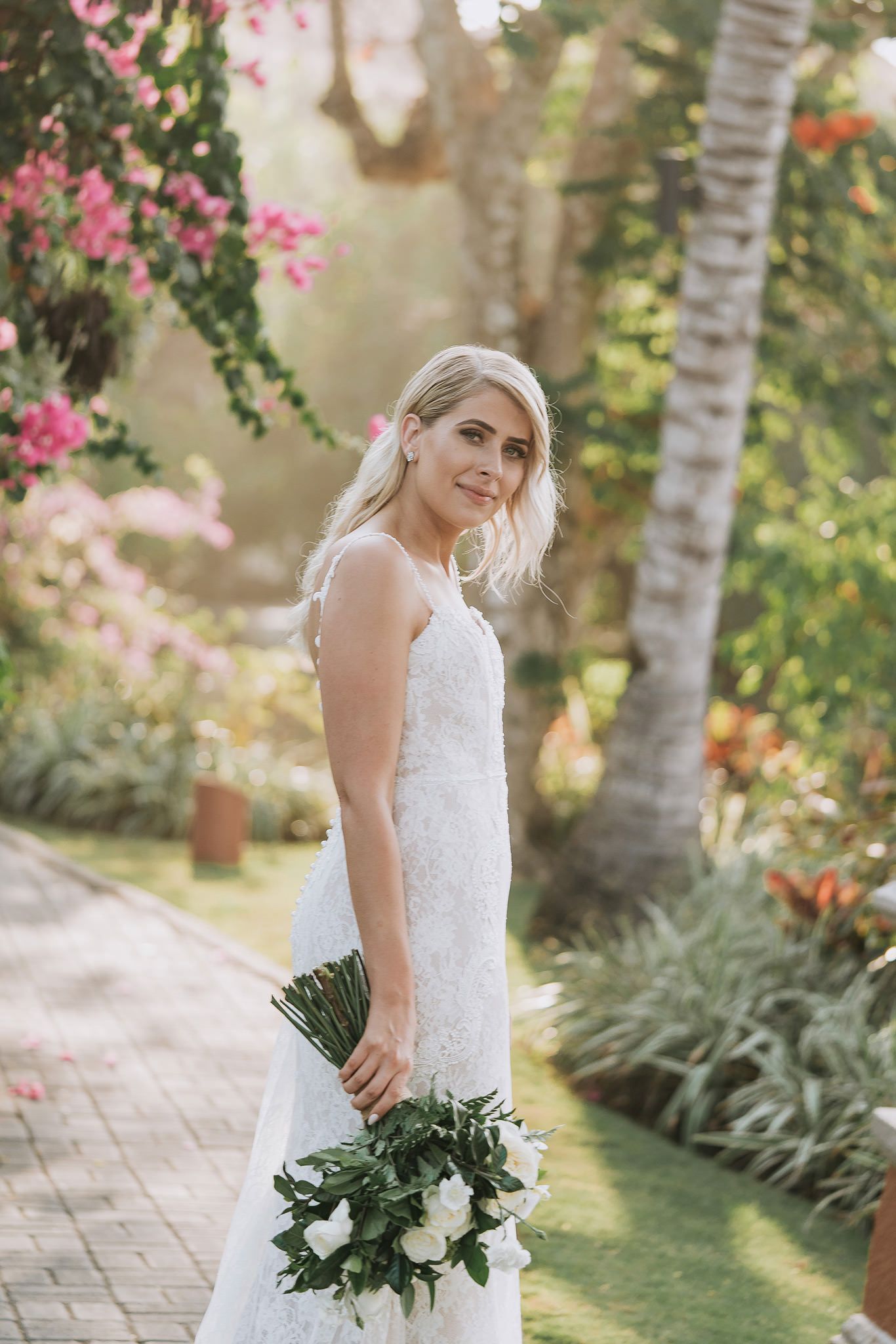 White lace wedding dress details in a tropical garden setting with pink bougainvillea flowers.