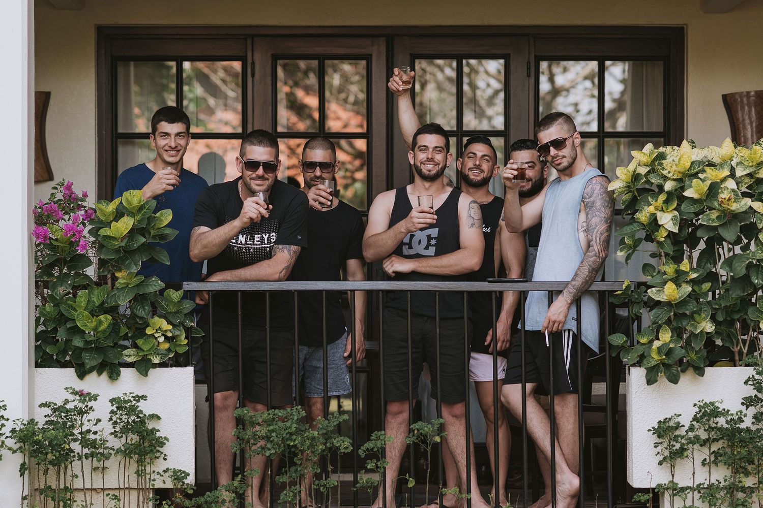 A group of friends gathered on a porch balcony with plants and flowers.
