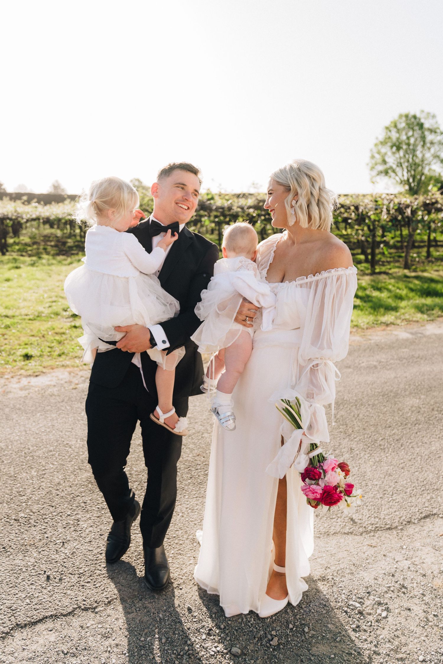 A couples special moment with little ones on a sunlit vineyard path.