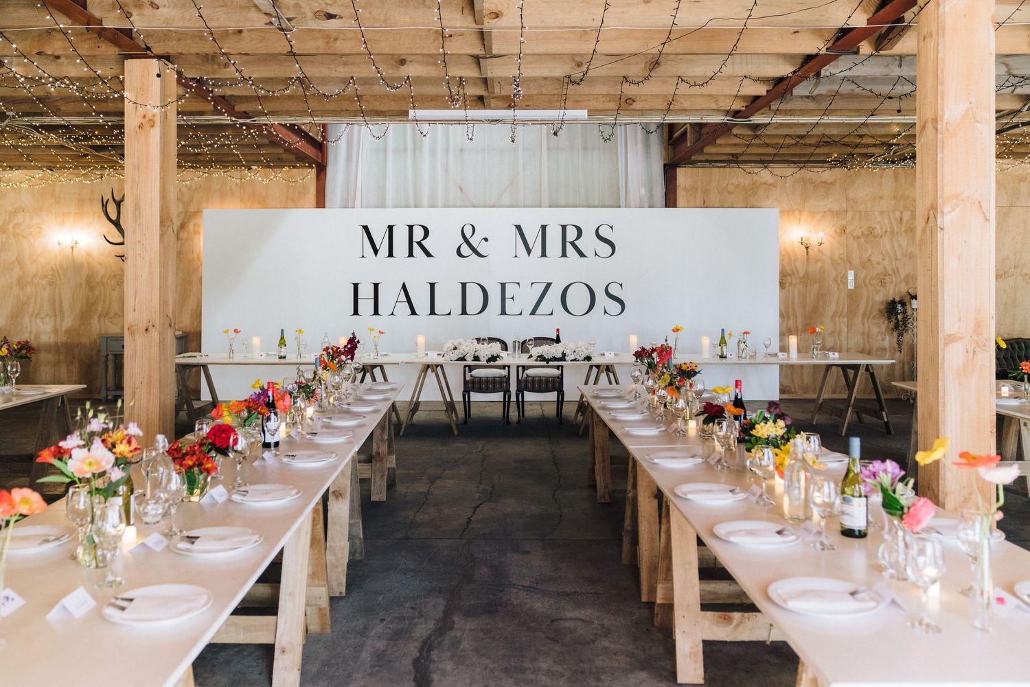 Elegant wedding reception tables arranged in long rows inside an industrial-style venue with exposed ceiling and columns.