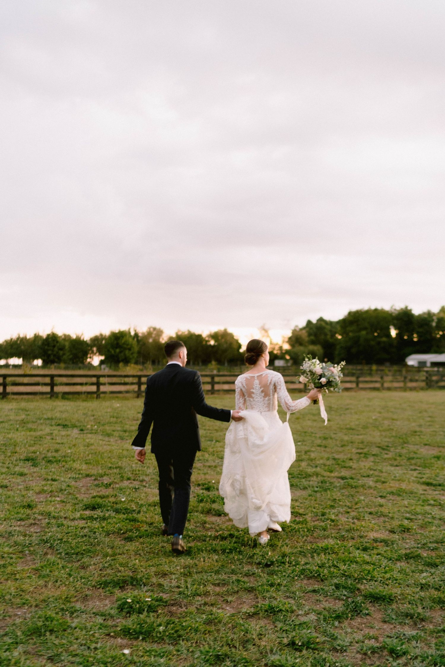 Couple walking through a pastoral field at sunset after their wedding ceremony.