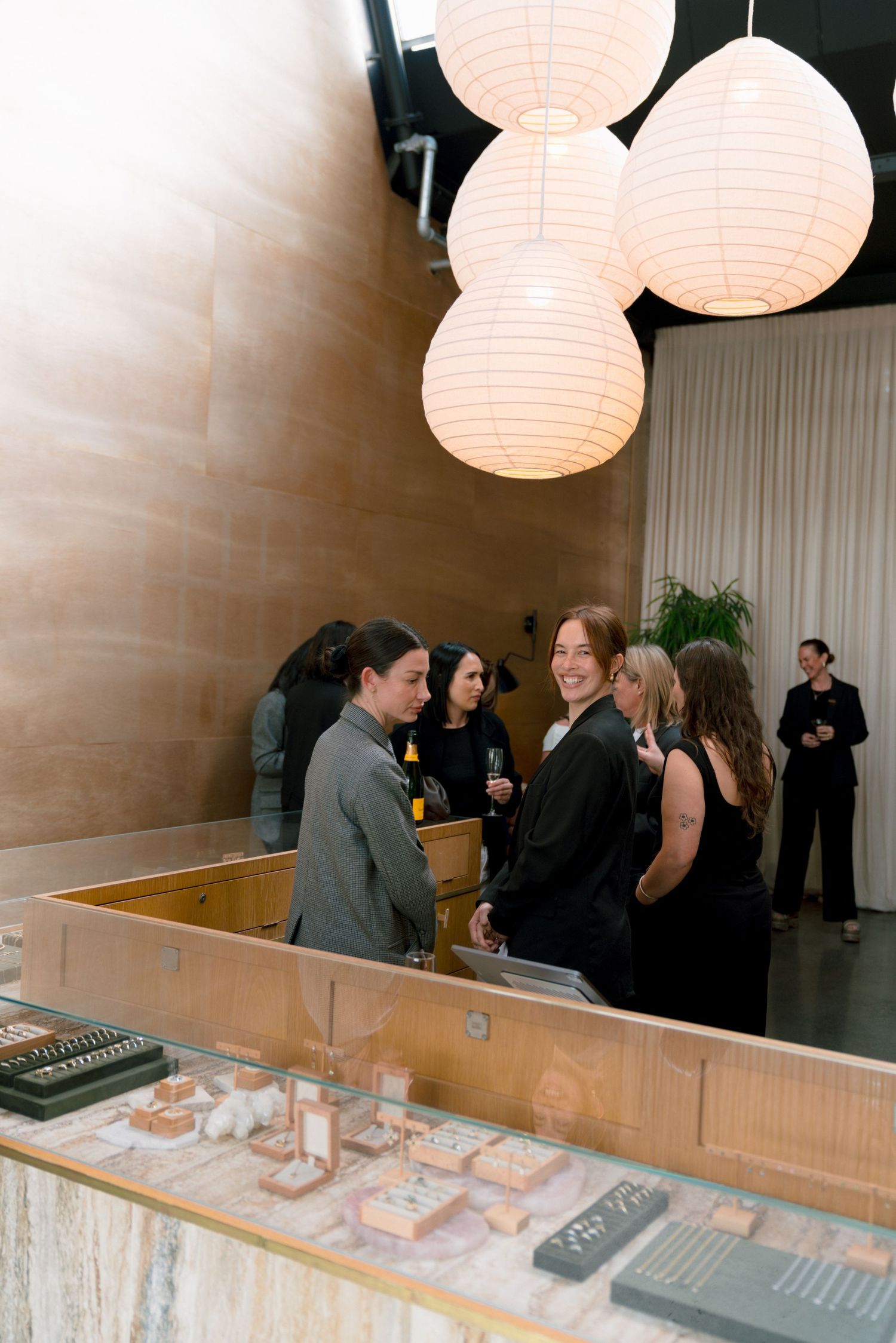 Guests mingle at an elegant jewelry store event under glowing paper lantern lights with display cases in foreground.
