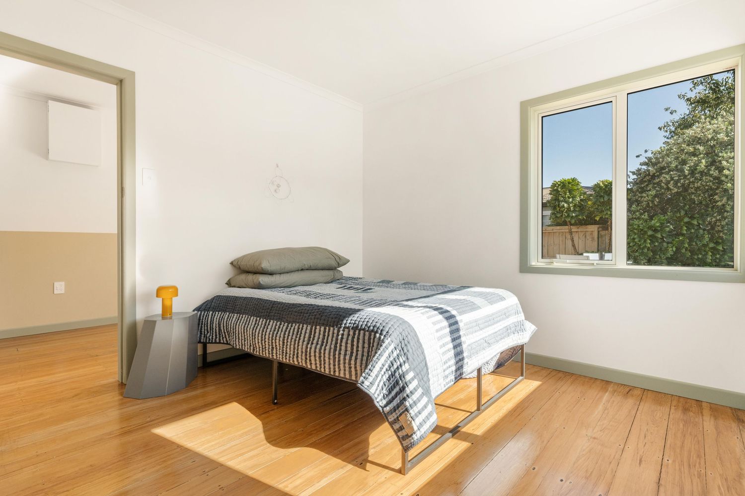 Spacious bedroom interior with hardwood floors and striped bedding near sunlit windows.