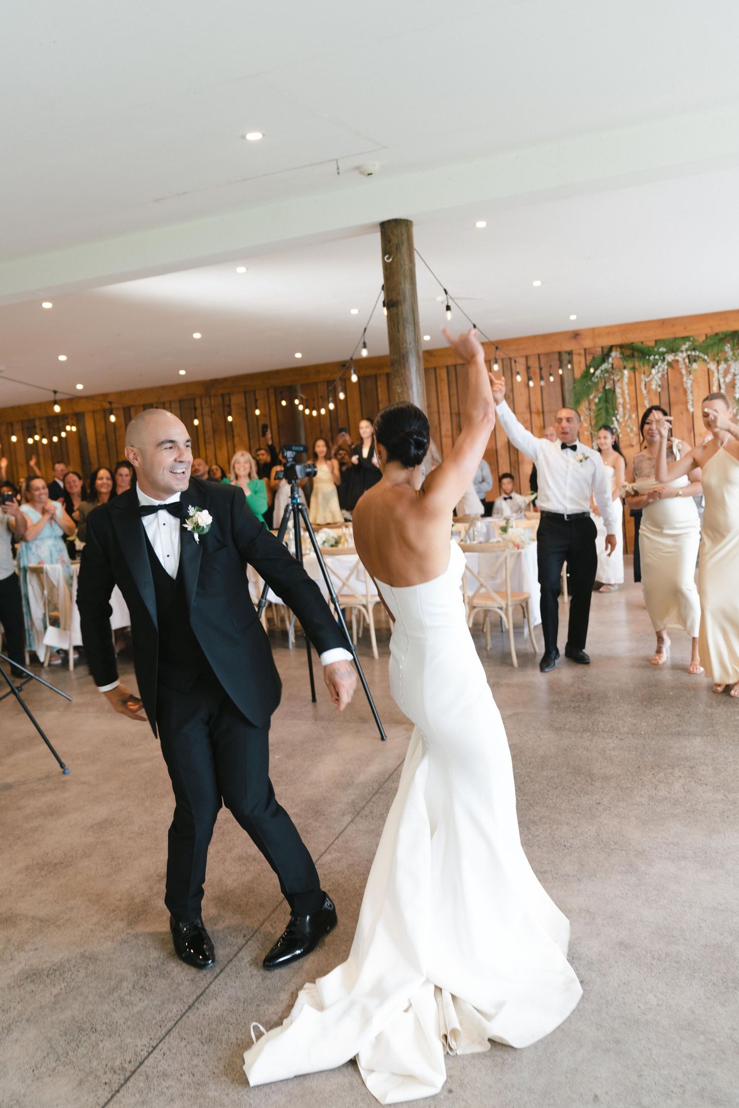 Wedding couple dancing and celebrating with guests in an indoor reception venue decorated with string lights.
