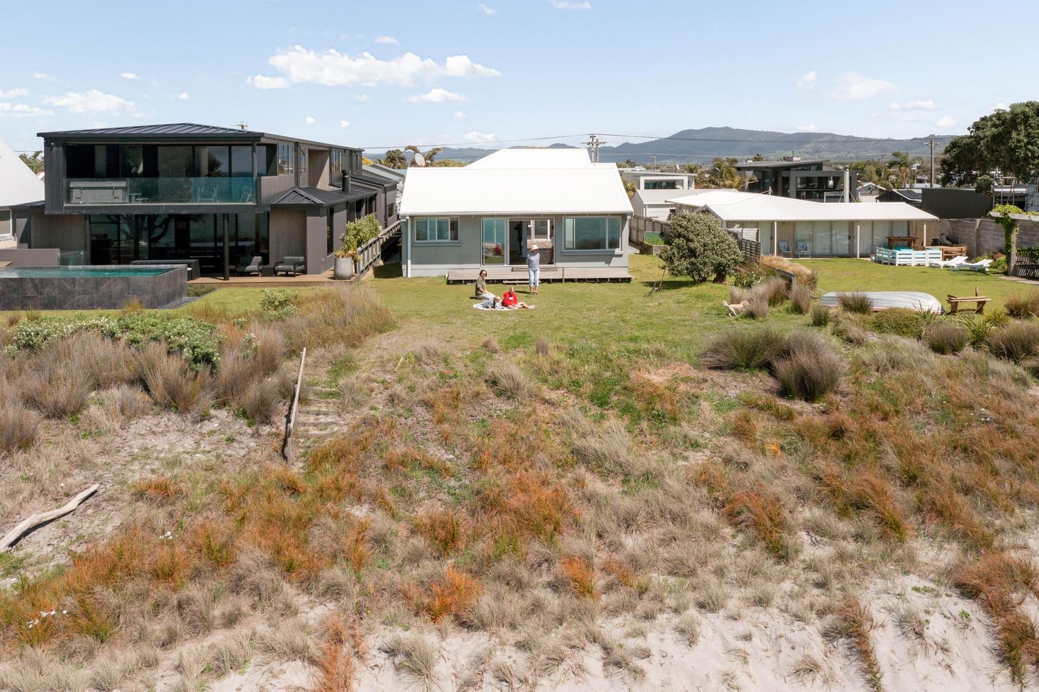 Panoramic view of modern coastal homes nestled along a rugged hillside with native brush and distant mountains.