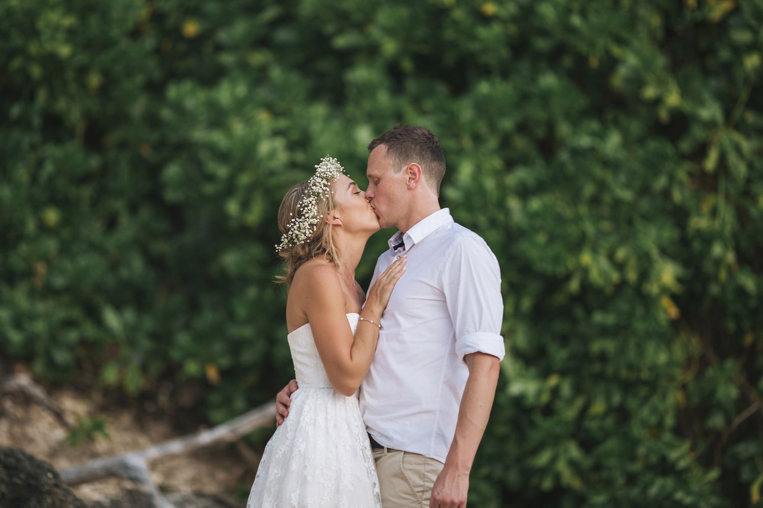 A romantic wedding couple shares intimate moments in a scenic outdoor setting with lush greenery.