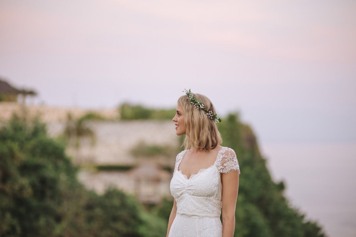 A woman in a white lace dress stands in an outdoor venue among natural surroundings during sunset.
