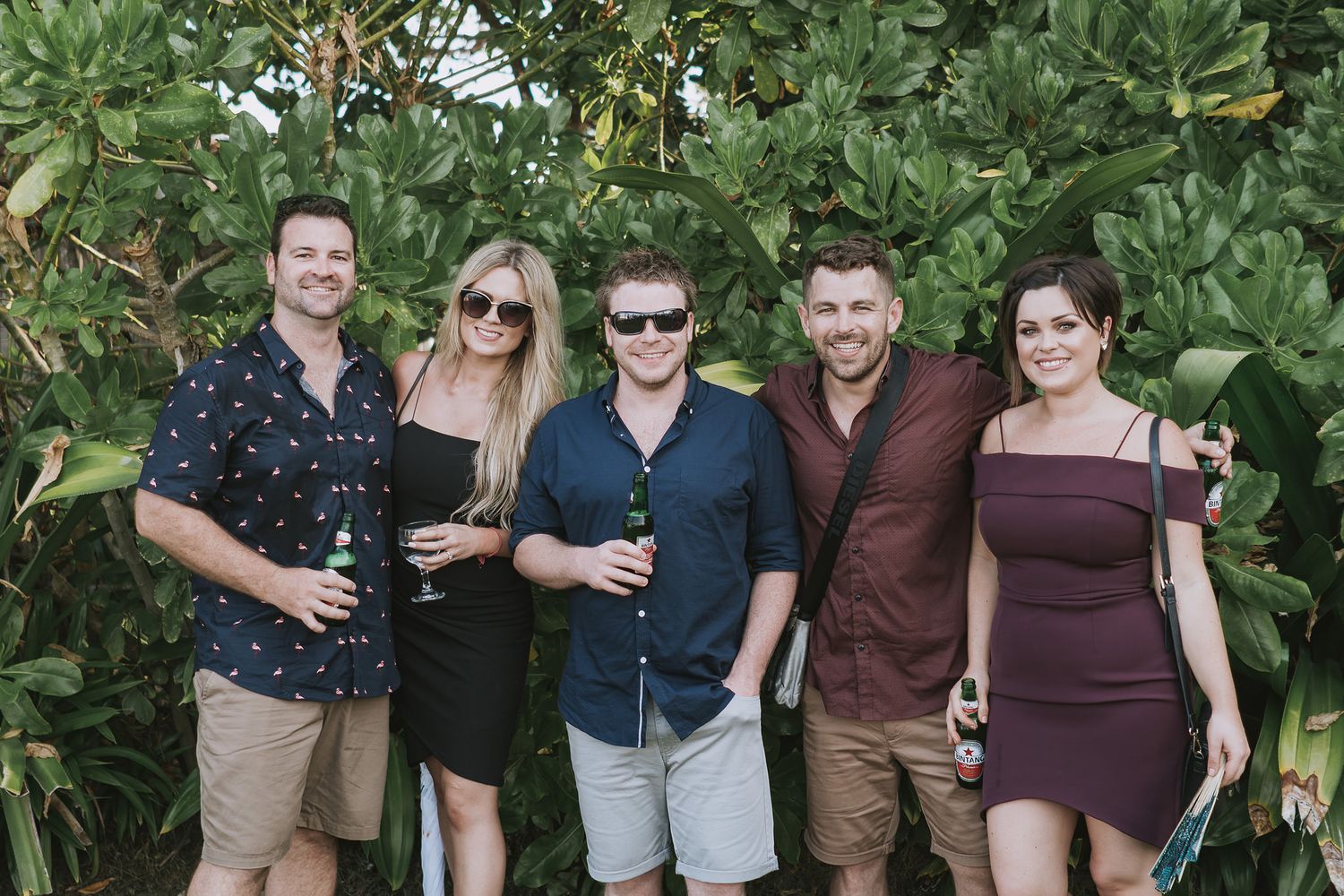 Friends pose together against tropical foliage at a social gathering.