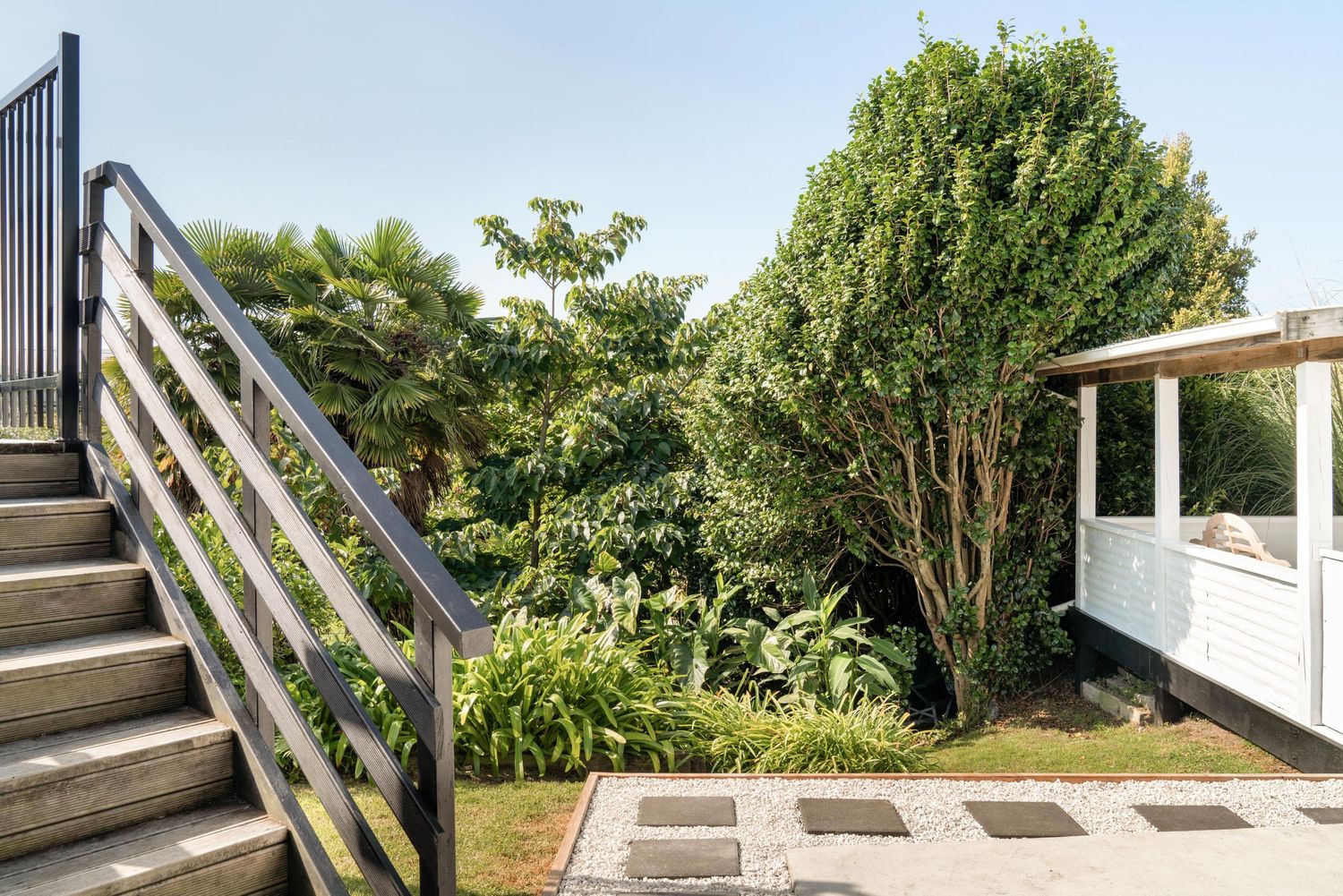 Modern wooden stairs lead up to a lush garden patio with greenery and landscaping.