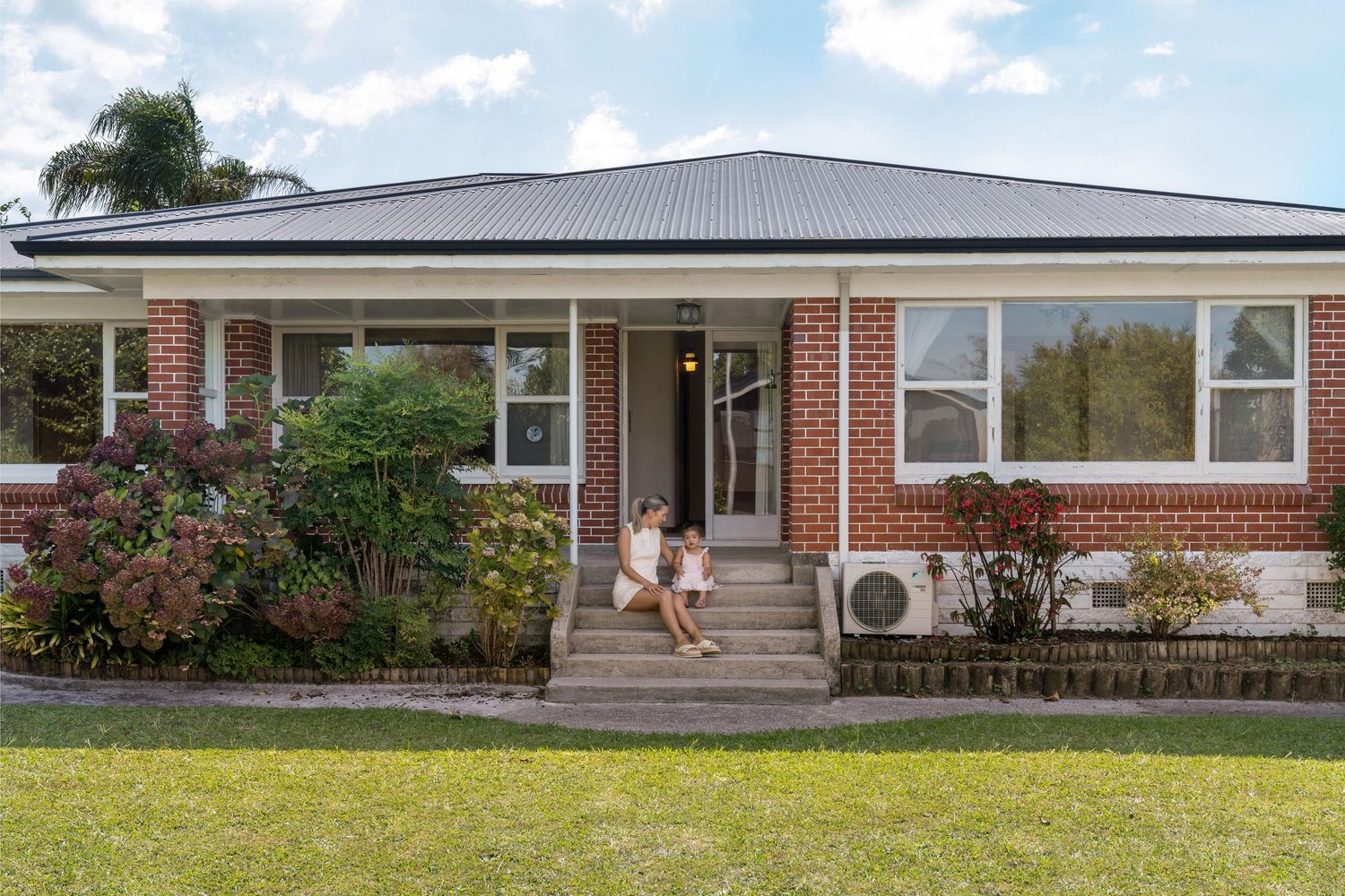 Single-story brick ranch house with gray metal roof and white trim features a covered front porch and neat landscaping.