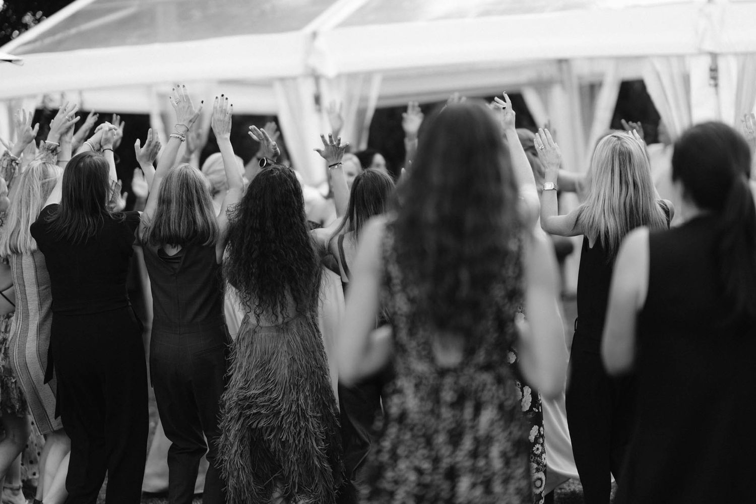 A black and white photo of people dancing under a tent at an elegant event with guests wearing formal attire.