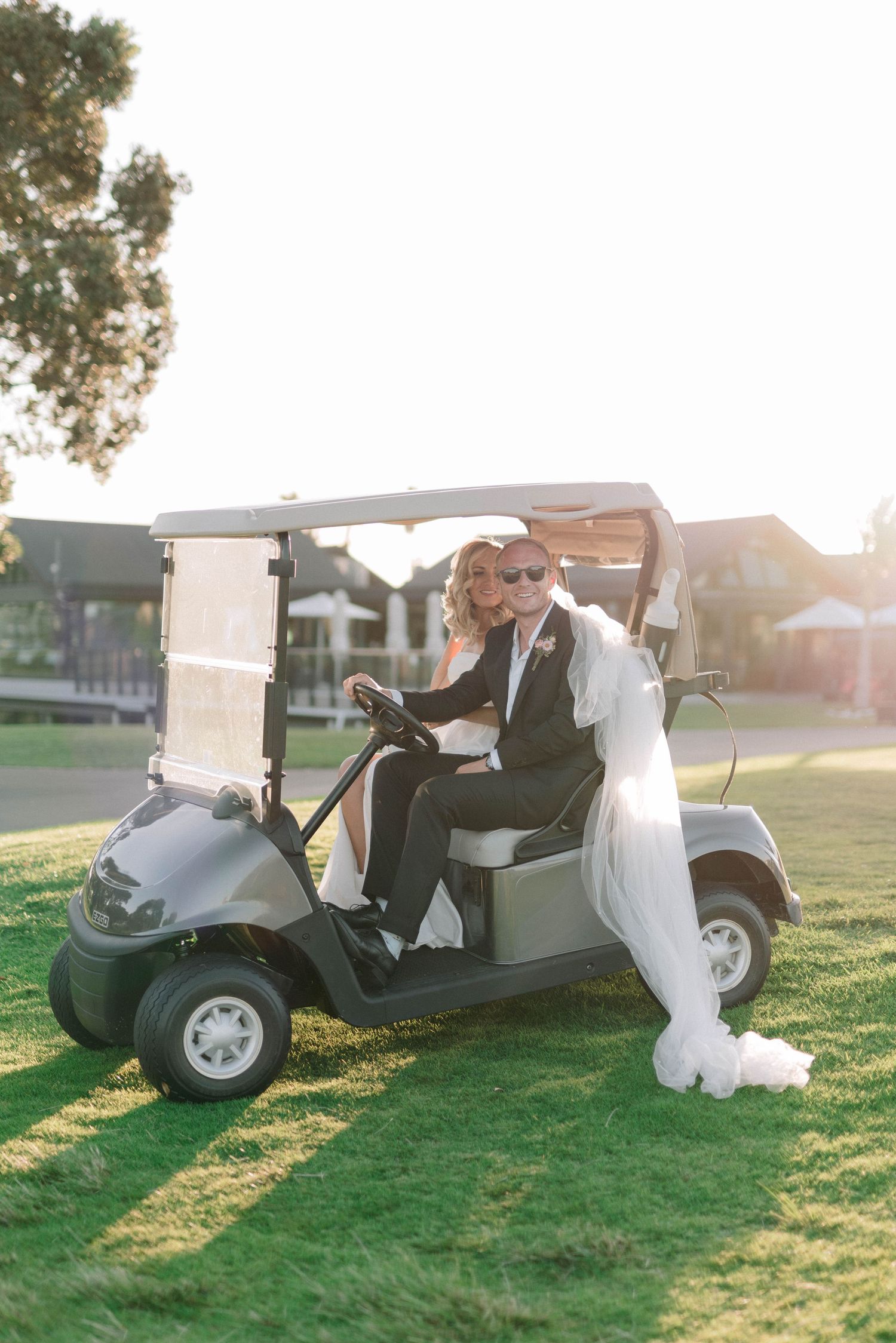 Golf cart rides during golden hour sunset at outdoor wedding venue on grassy course.