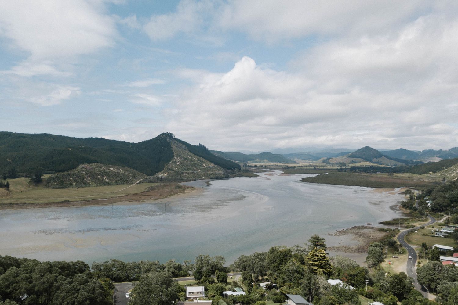 A scenic panoramic view of a winding coastline with mountains and calm waters under partly cloudy skies.