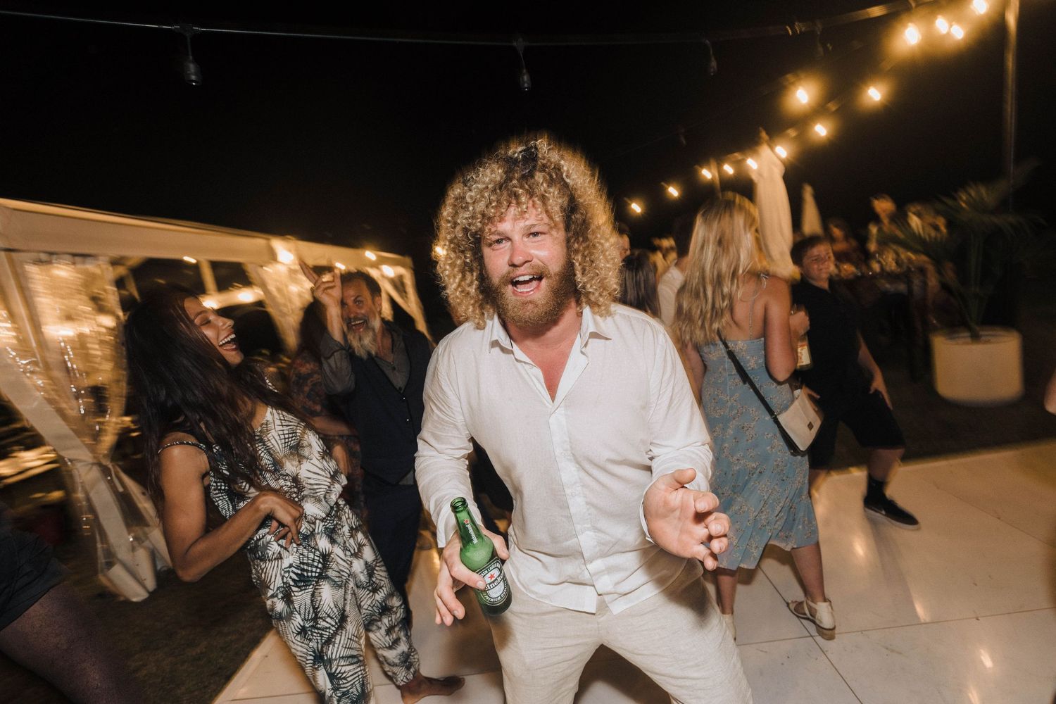 Wedding guest dancing enthusiastically at outdoor reception under string lights.