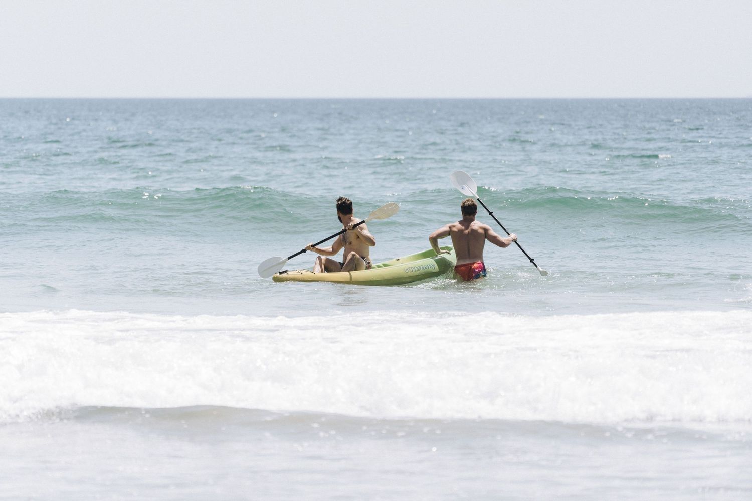 Two lifeguards rowing a yellow rescue boat through ocean waves at the beach during patrol.