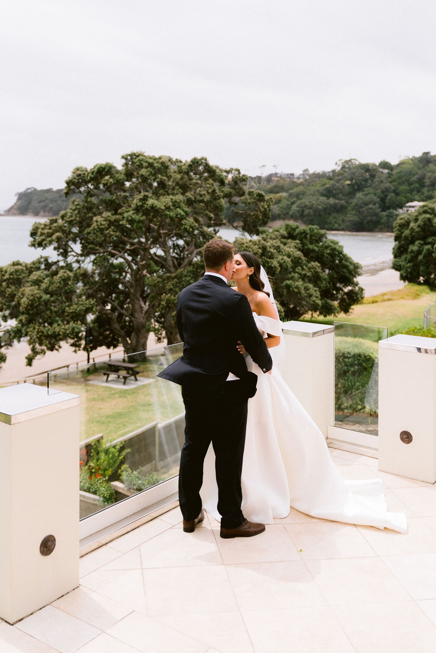 A romantic moment captured on a white balcony overlooking a scenic coastal view on a cloudy day.