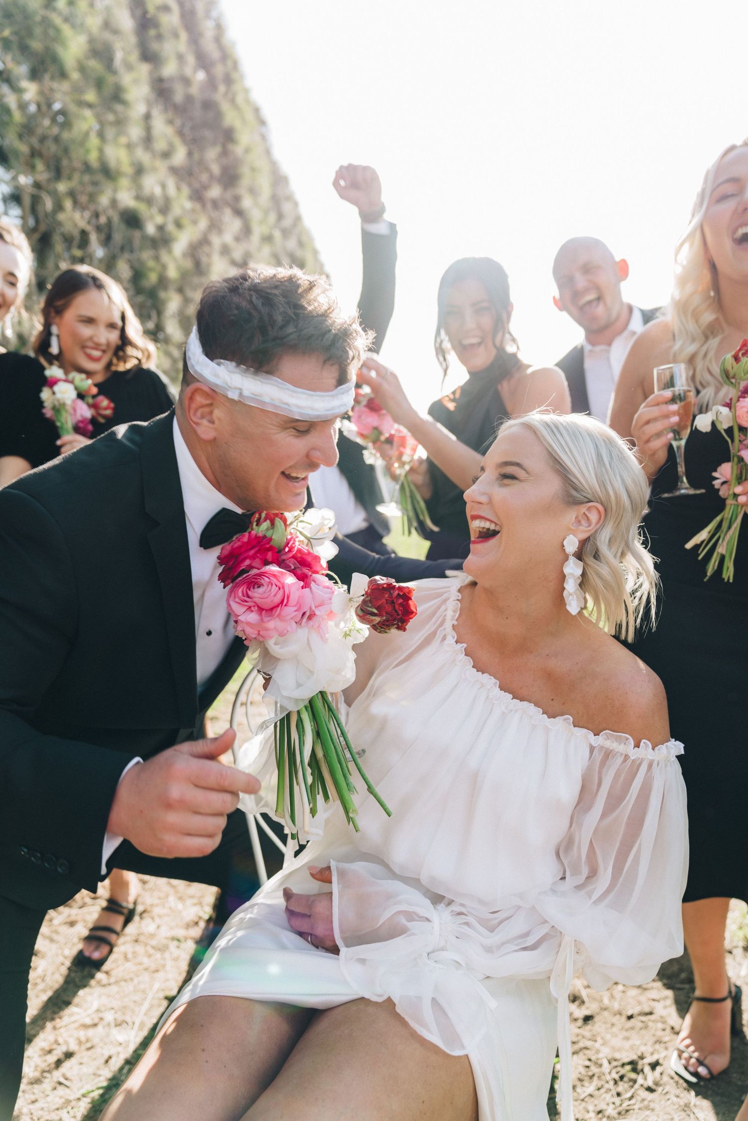Joyful celebration with white attire and pink floral bouquet against scenic outdoor backdrop.
