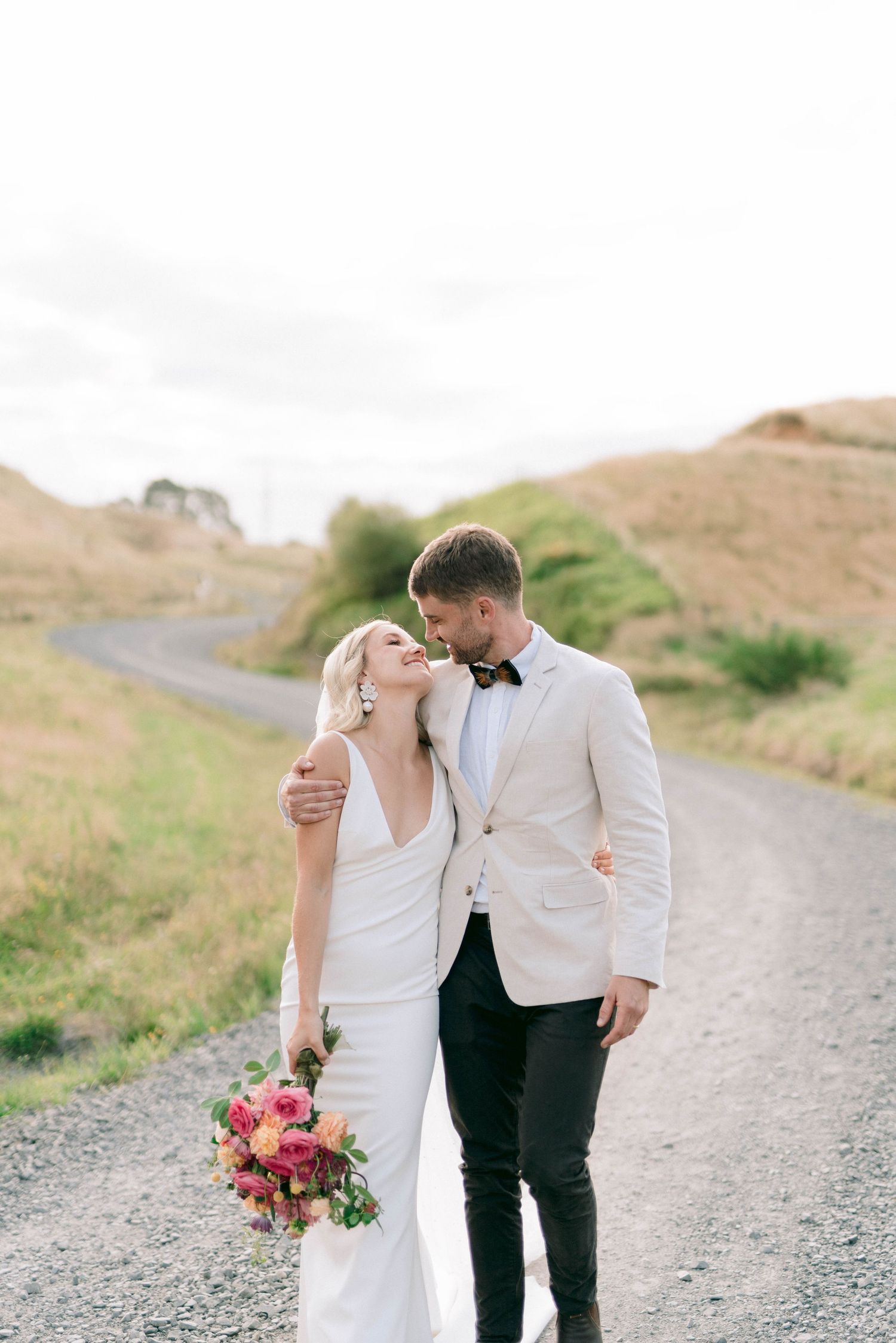Romantic wedding photos on a gravel path with pink floral bouquet and rolling hills.