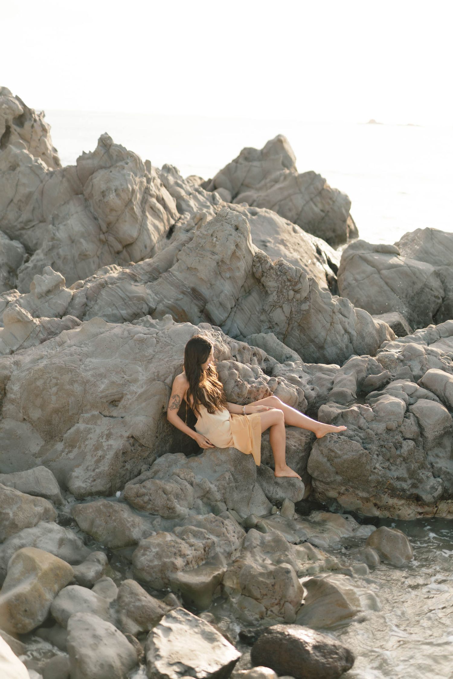 Model poses elegantly on rocky coastal formation during sunset.