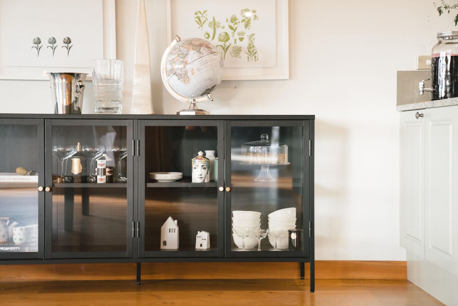A black metal and glass display cabinet showcases decorative items including a globe, glassware and ceramic pieces.