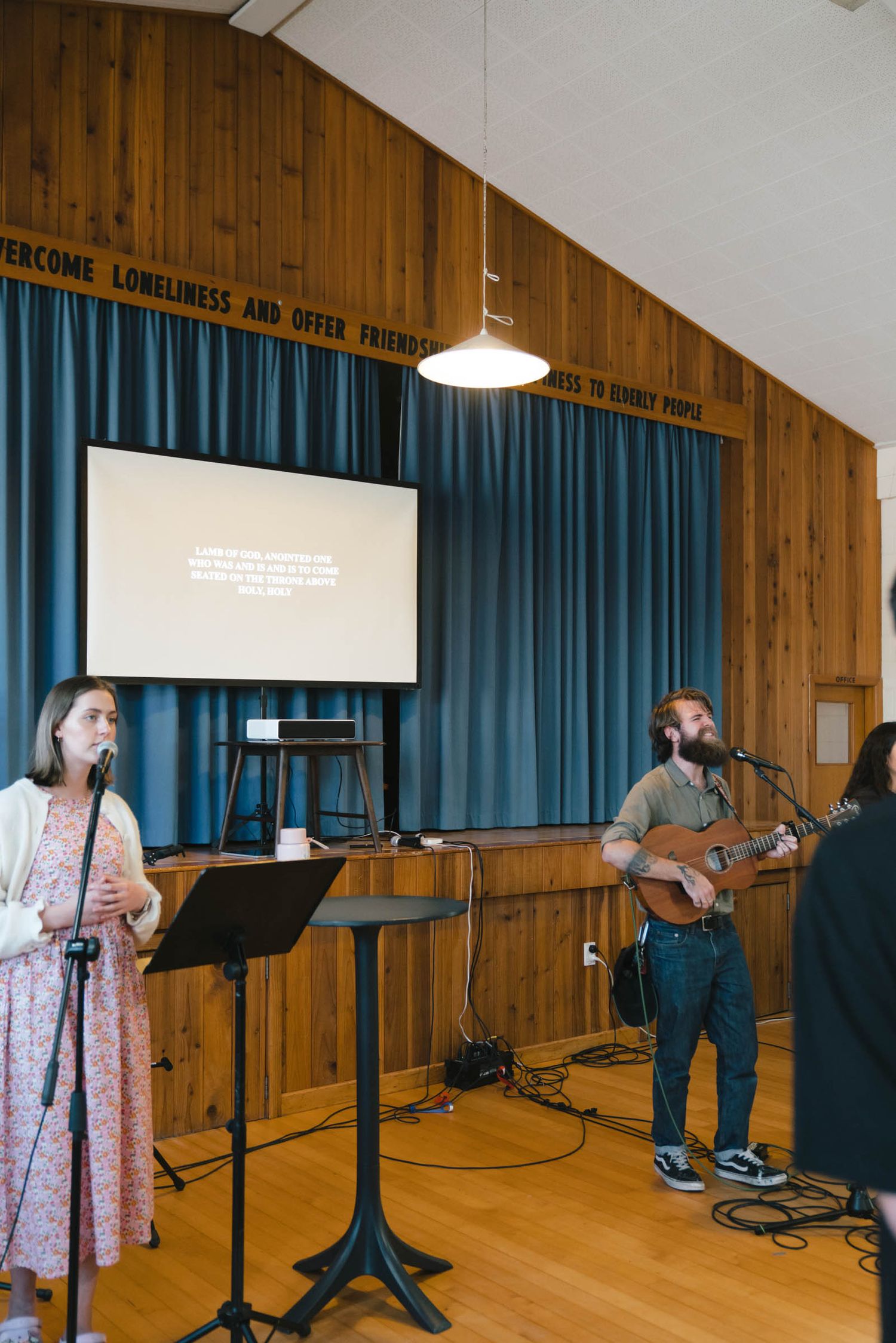Performance space with wooden walls, blue curtains, and music equipment set up.