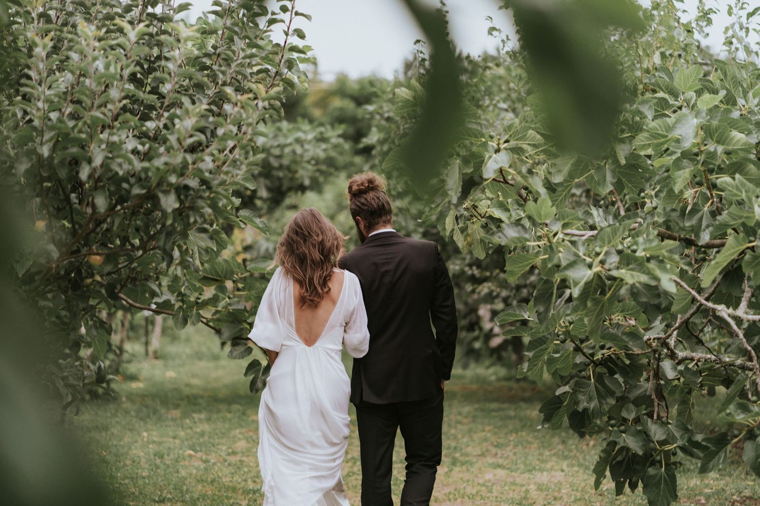 Newlywed couple walks together through an apple orchard on their wedding day.