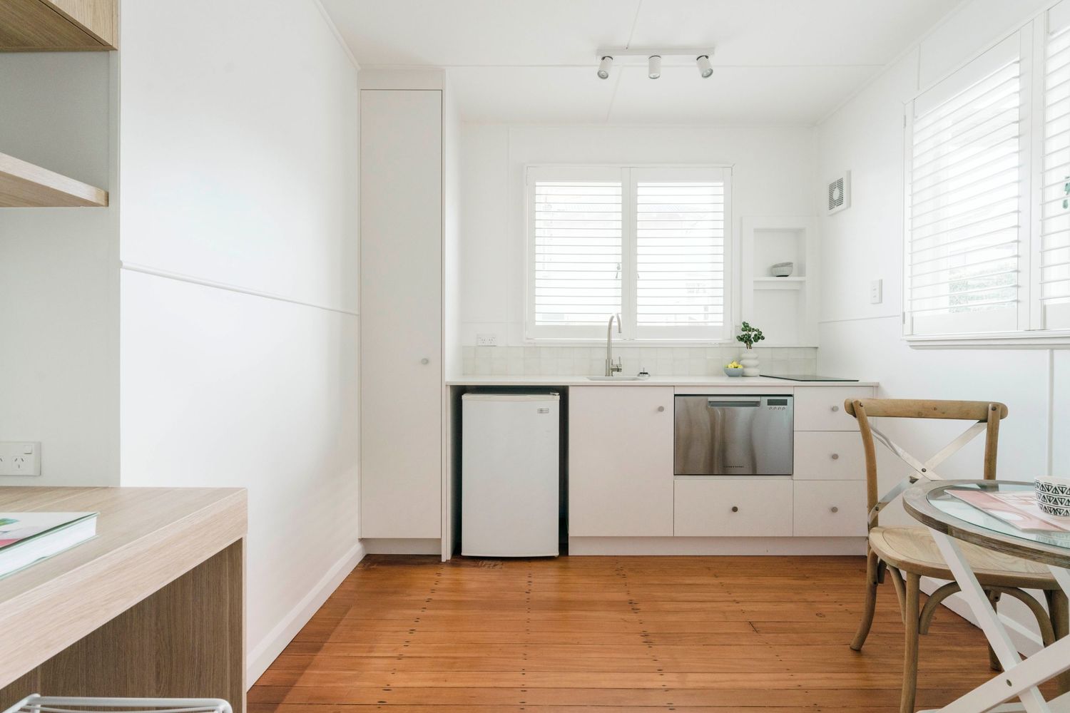 Minimalist white kitchen with wooden floors, built-in appliances and a small dining area.