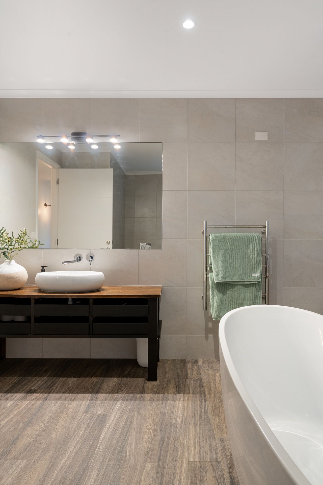 Modern bathroom with floating wooden vanity, vessel sink, and freestanding tub on wood-look floors.