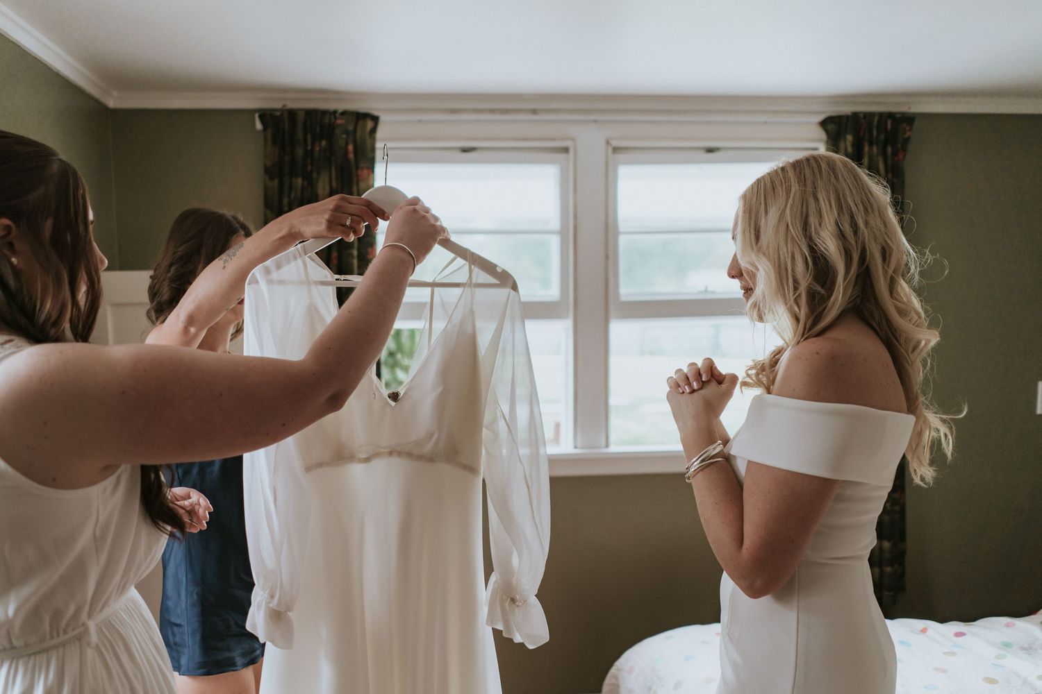 Wedding preparation scene in a room with hanging white dress and soft natural window light.