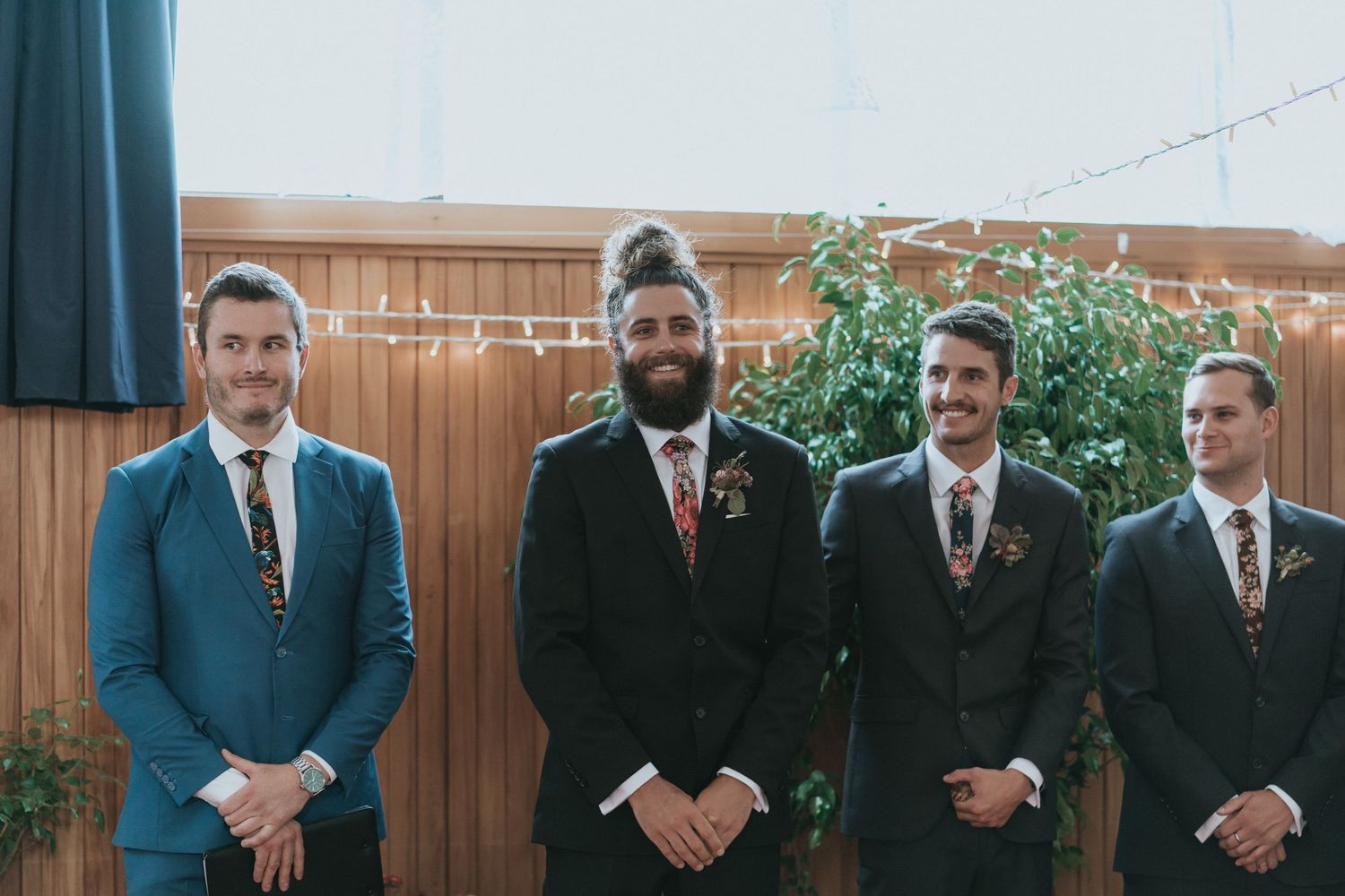 A group of formally dressed wedding party members stand together in matching navy suits and ties.