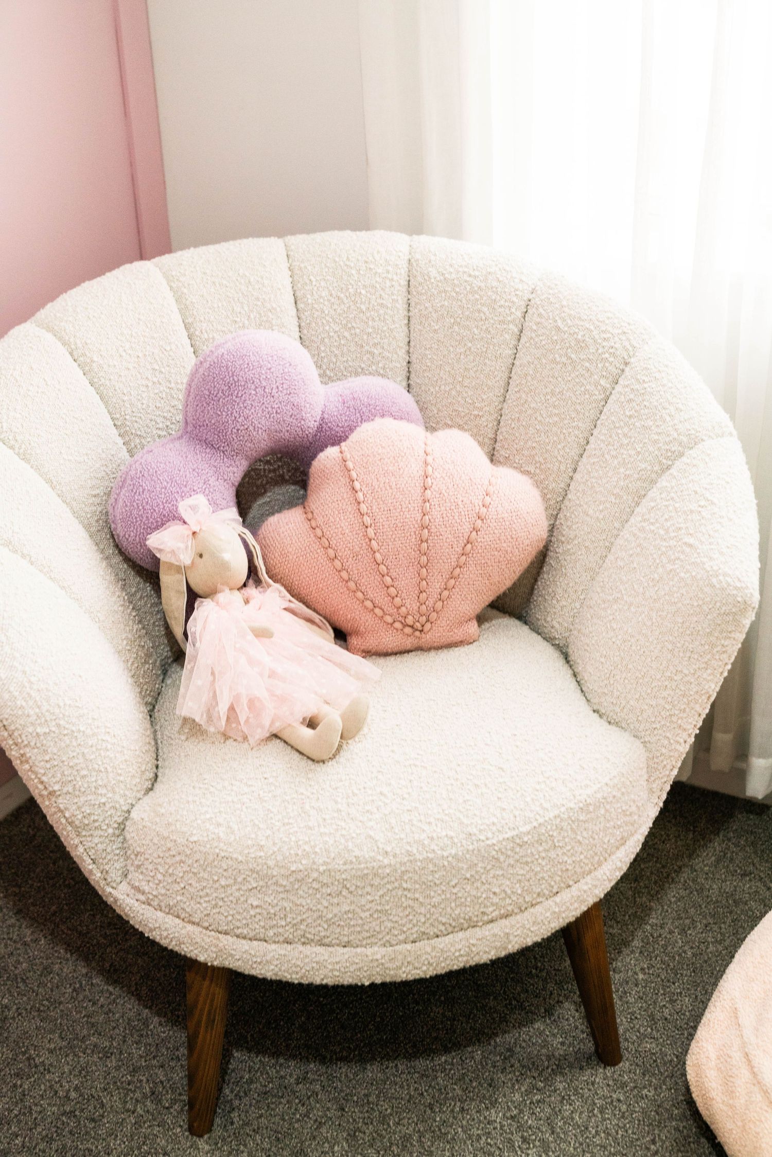 Round cream-colored retro chair with pink and purple shell-shaped pillows on dark carpet.