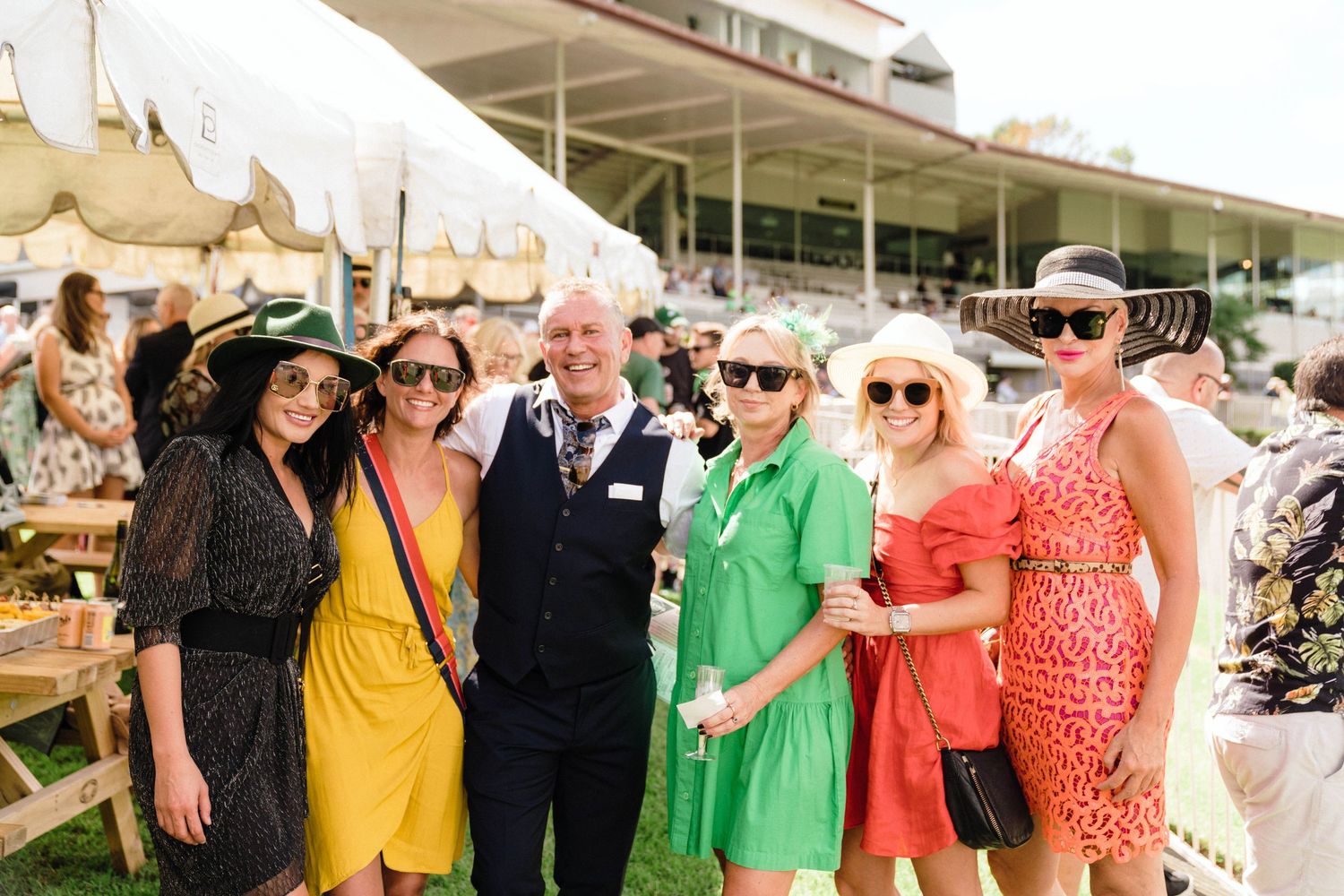 A group of well-dressed guests mingle and socialize at an outdoor event on a sunny day.