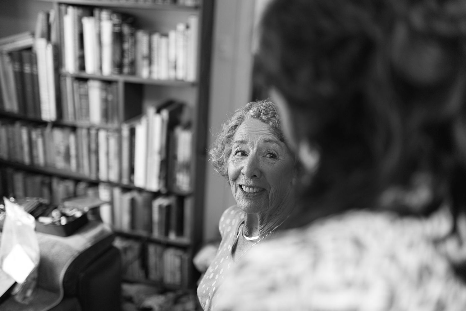 A candid black and white photo capturing a joyful moment in front of a bookshelf.