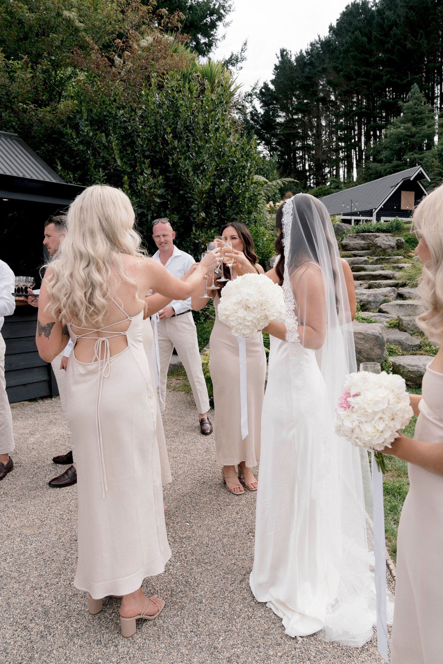 A wedding party walking outdoors in light colored dresses carrying white bouquets of flowers.