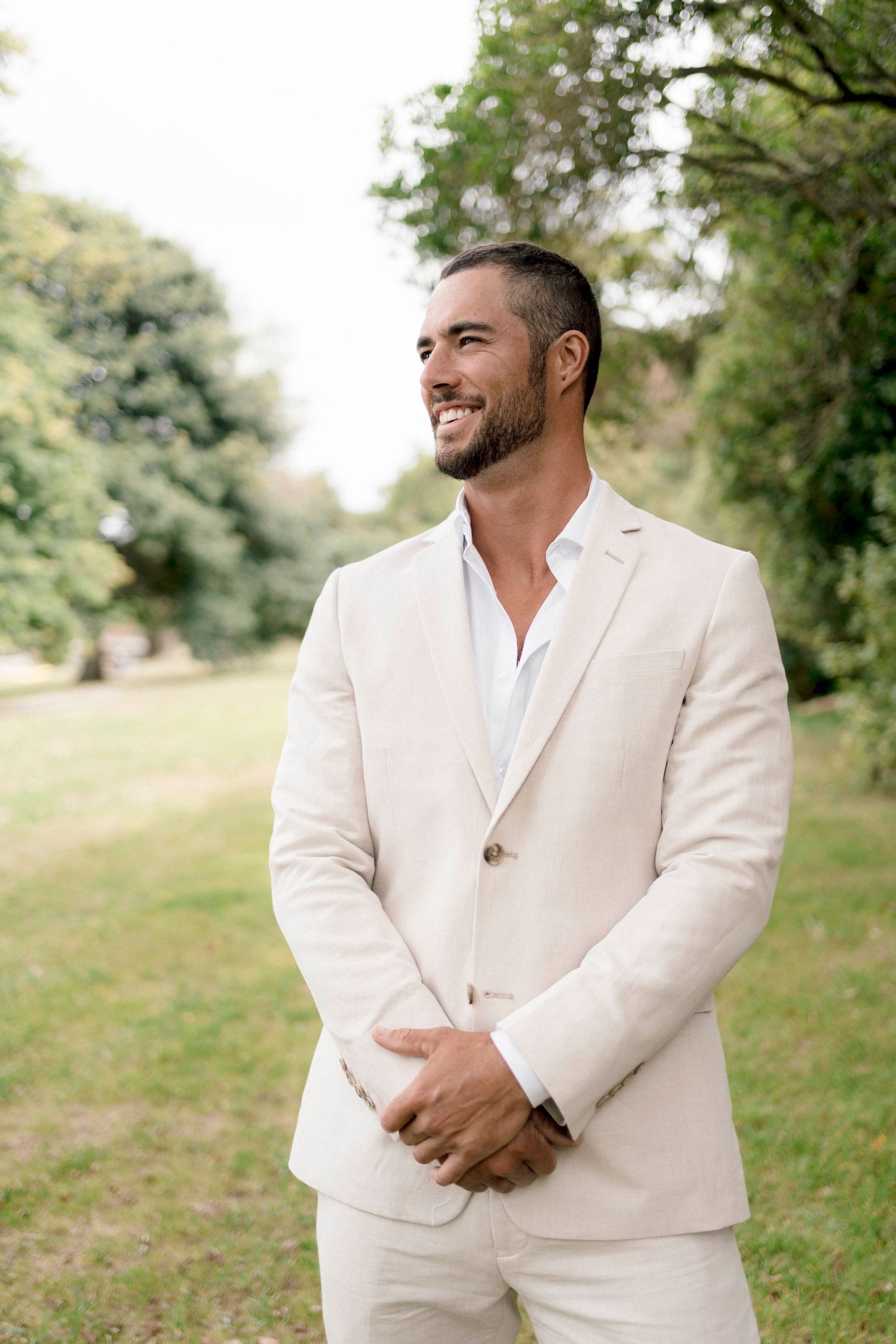 Person in cream linen suit smiling while standing in a sunny garden setting.