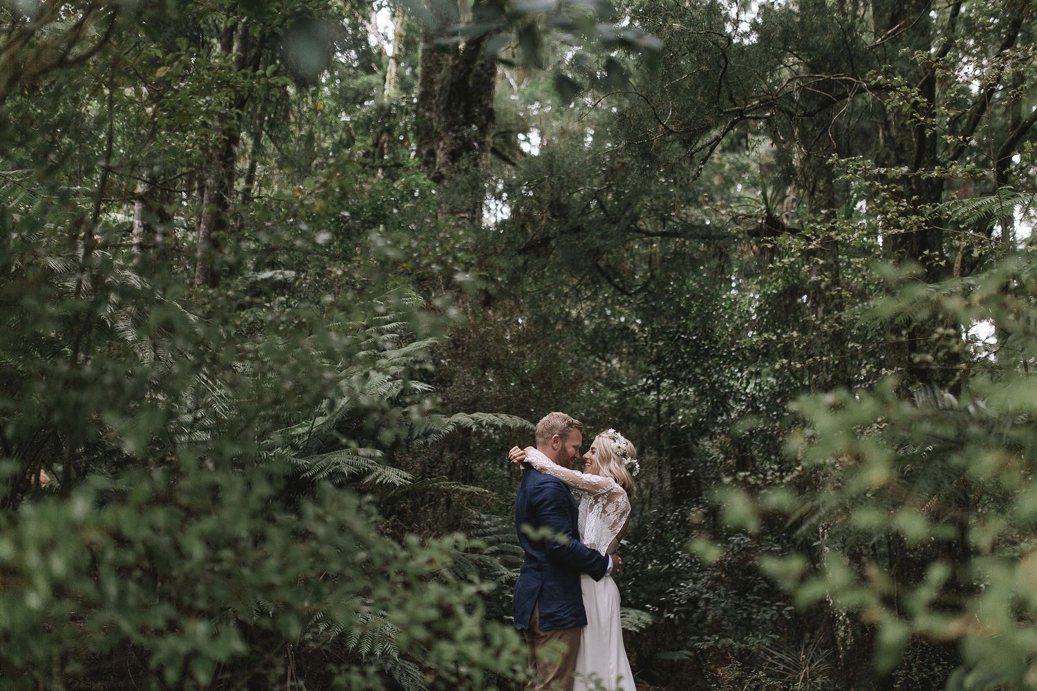 A couple shares a tender moment together in a lush wooded forest setting with soft natural lighting.