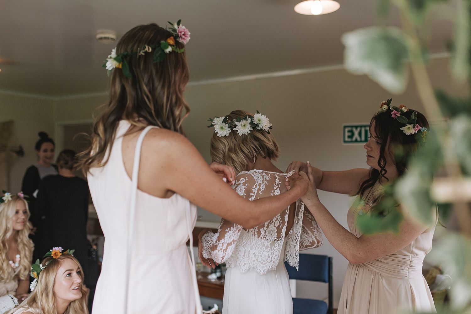 Three people in white dresses dance together at an indoor event with floral hair accessories.
