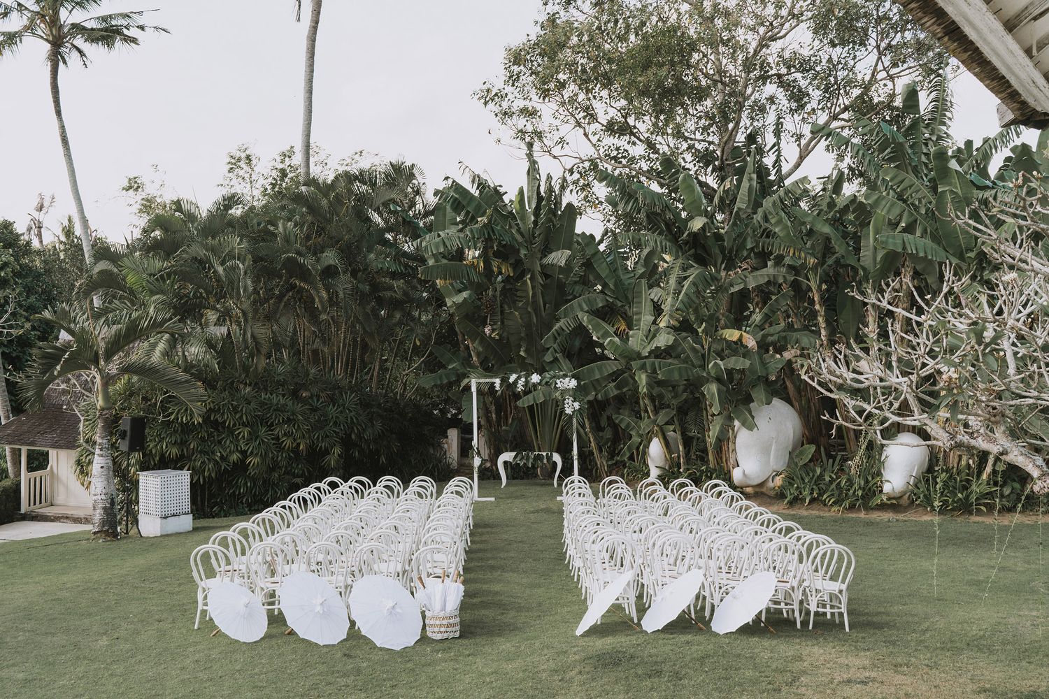 White chairs arranged in rows on a lush green lawn for an outdoor garden ceremony setup.