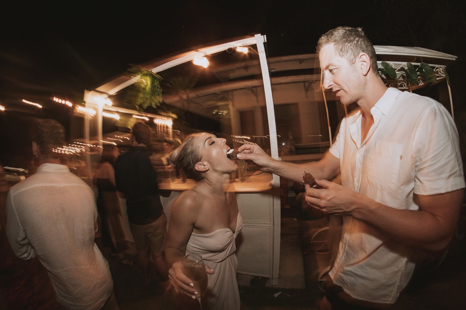 Guests share a lively moment at an outdoor evening wedding reception.