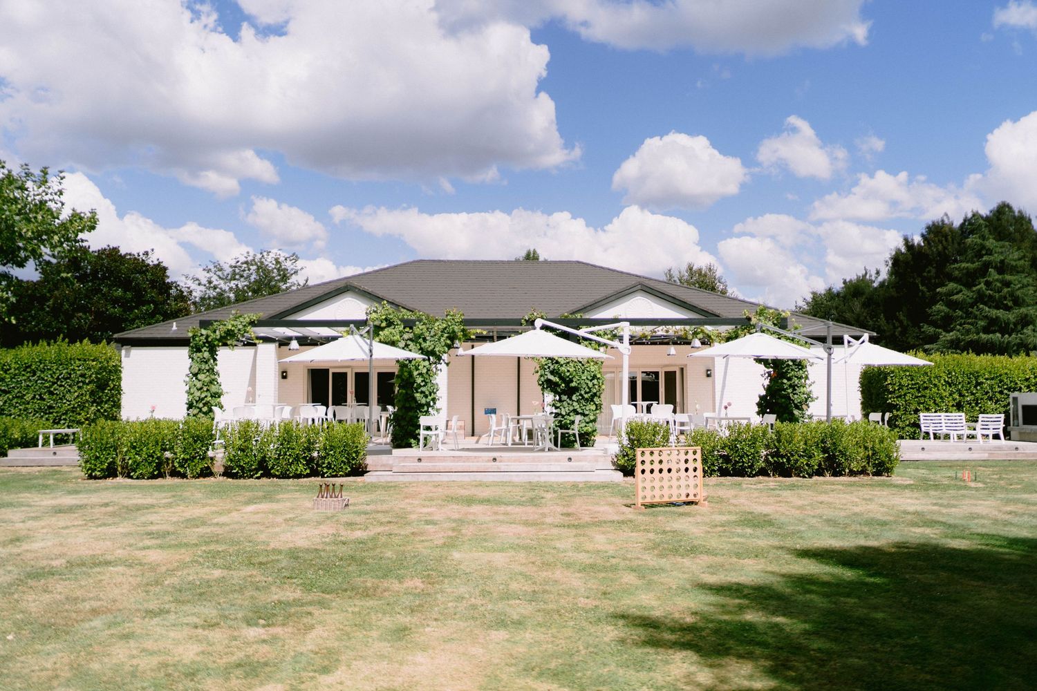 A panoramic view of a single-story building complex with manicured lawns and white fencing under a partly cloudy sky.