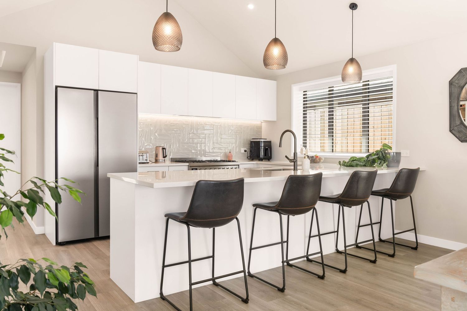 Contemporary white kitchen with black bar stools, copper pendant lights and large center island.