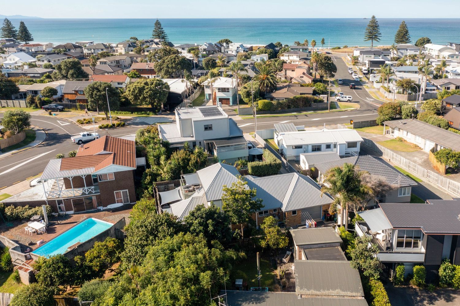 Aerial view of coastal suburban homes with swimming pools near beach in seaside neighborhood on sunny day.