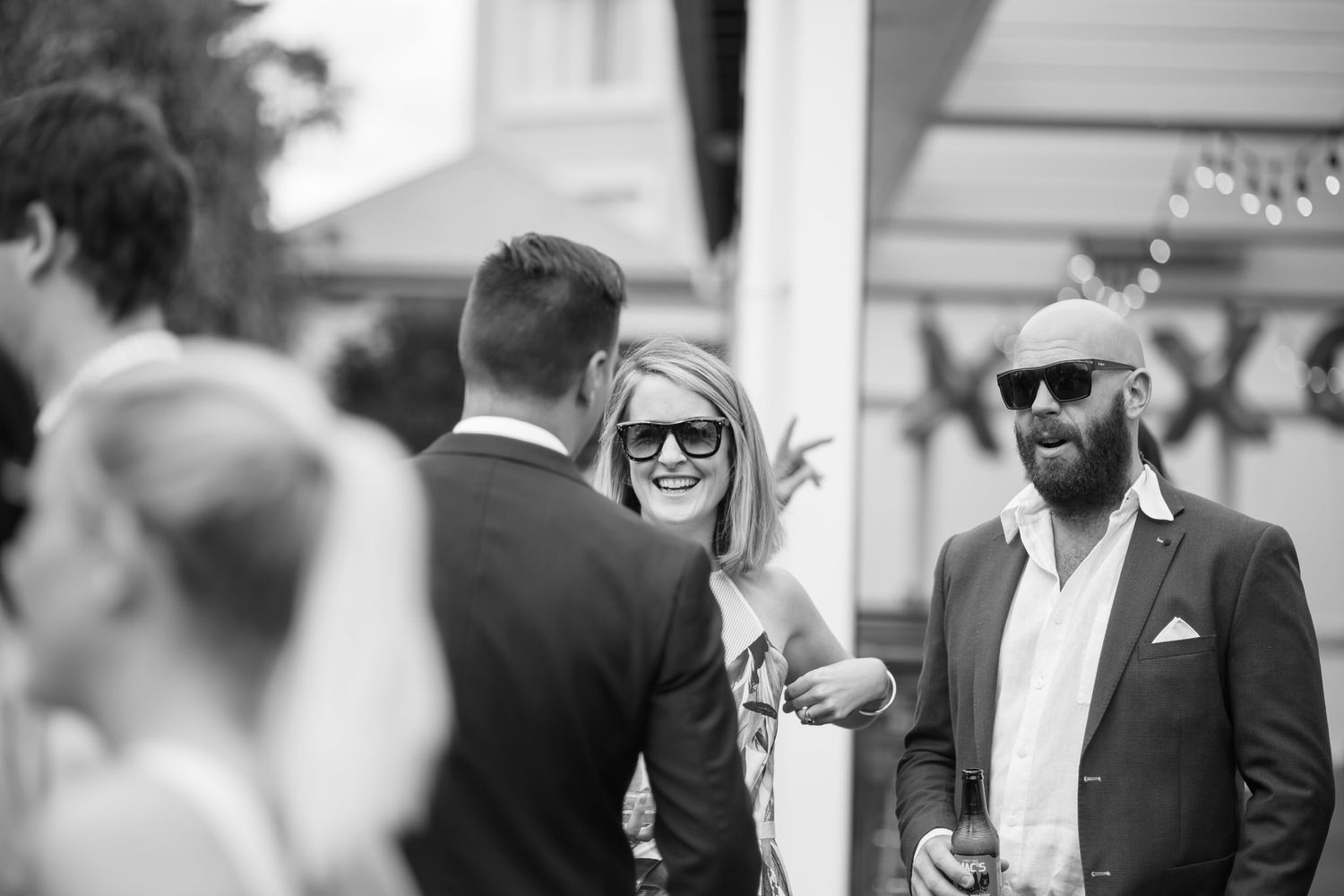 Black and white photo of wedding guests in formal attire socializing at an outdoor reception.