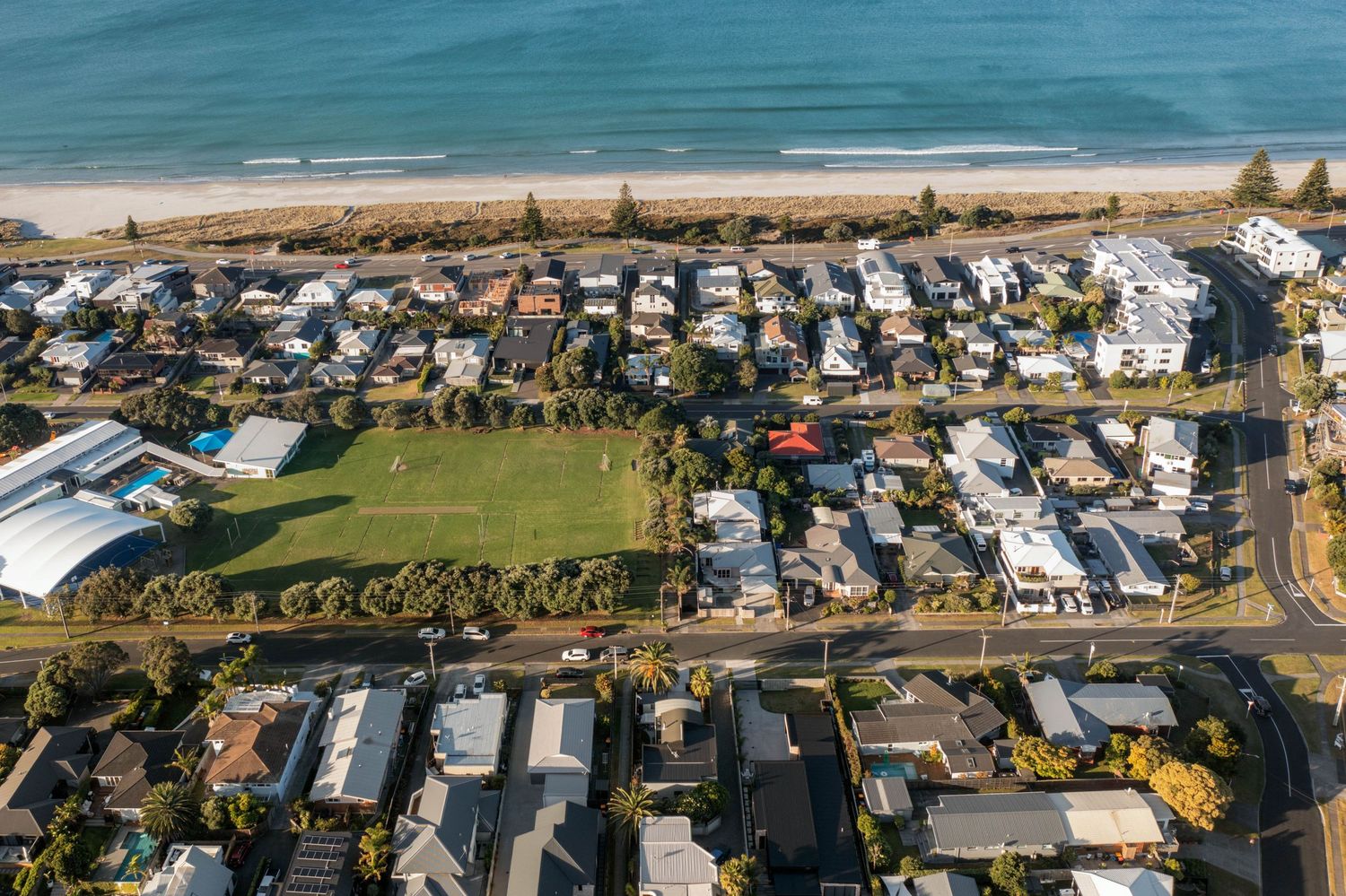Bird's eye view of beachfront homes and caravan park along the coastline with green spaces.
