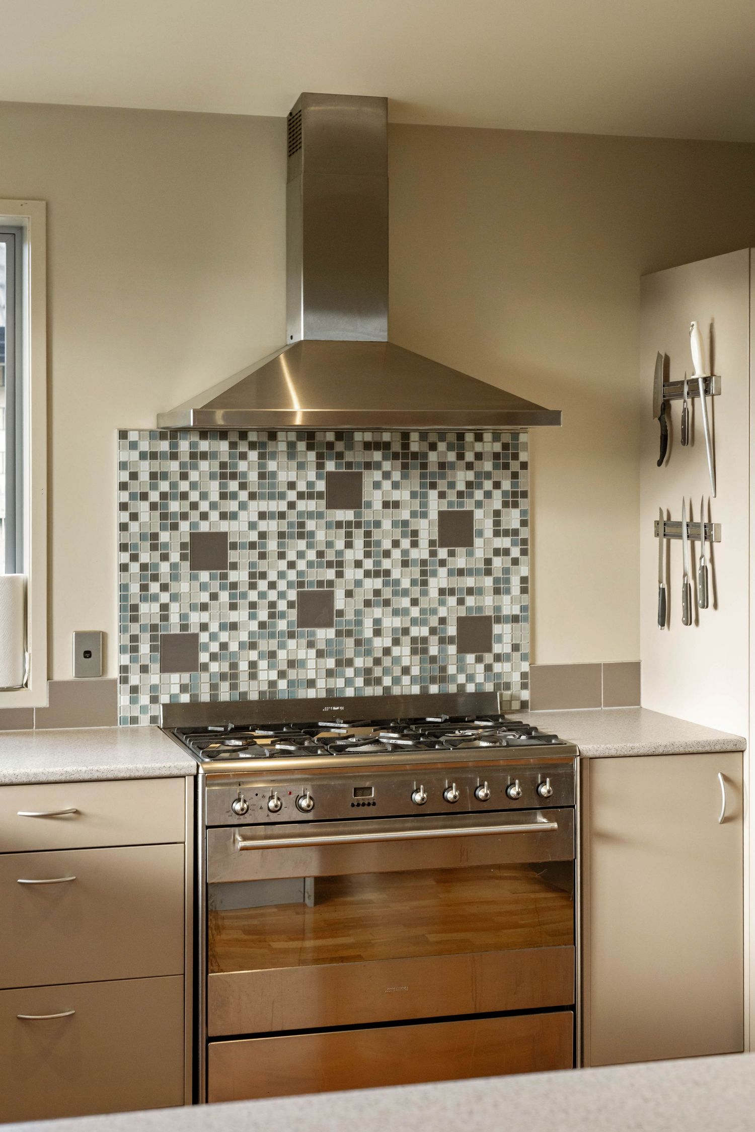 Modern kitchen featuring stainless steel range hood and mosaic tile backsplash with grey and white geometric pattern.