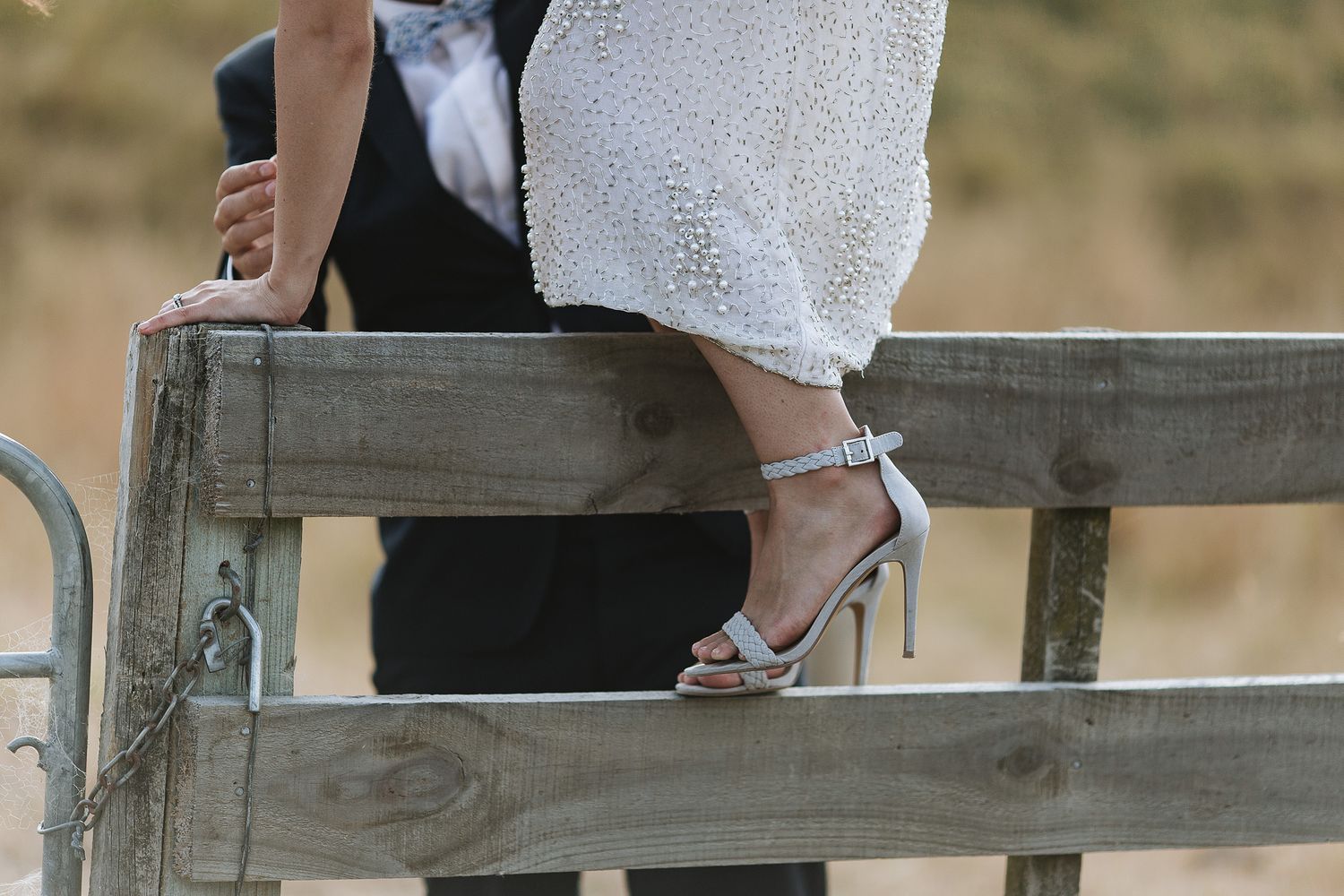 Close-up view of silver strappy high heel sandal on rustic wooden fence in outdoor setting.