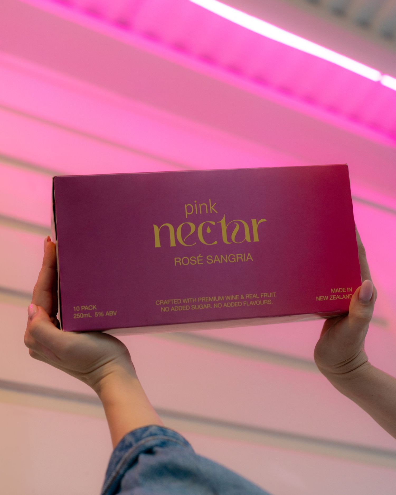 A box of Pink Nectar Rose Sangria being held against a pink neon-lit background.