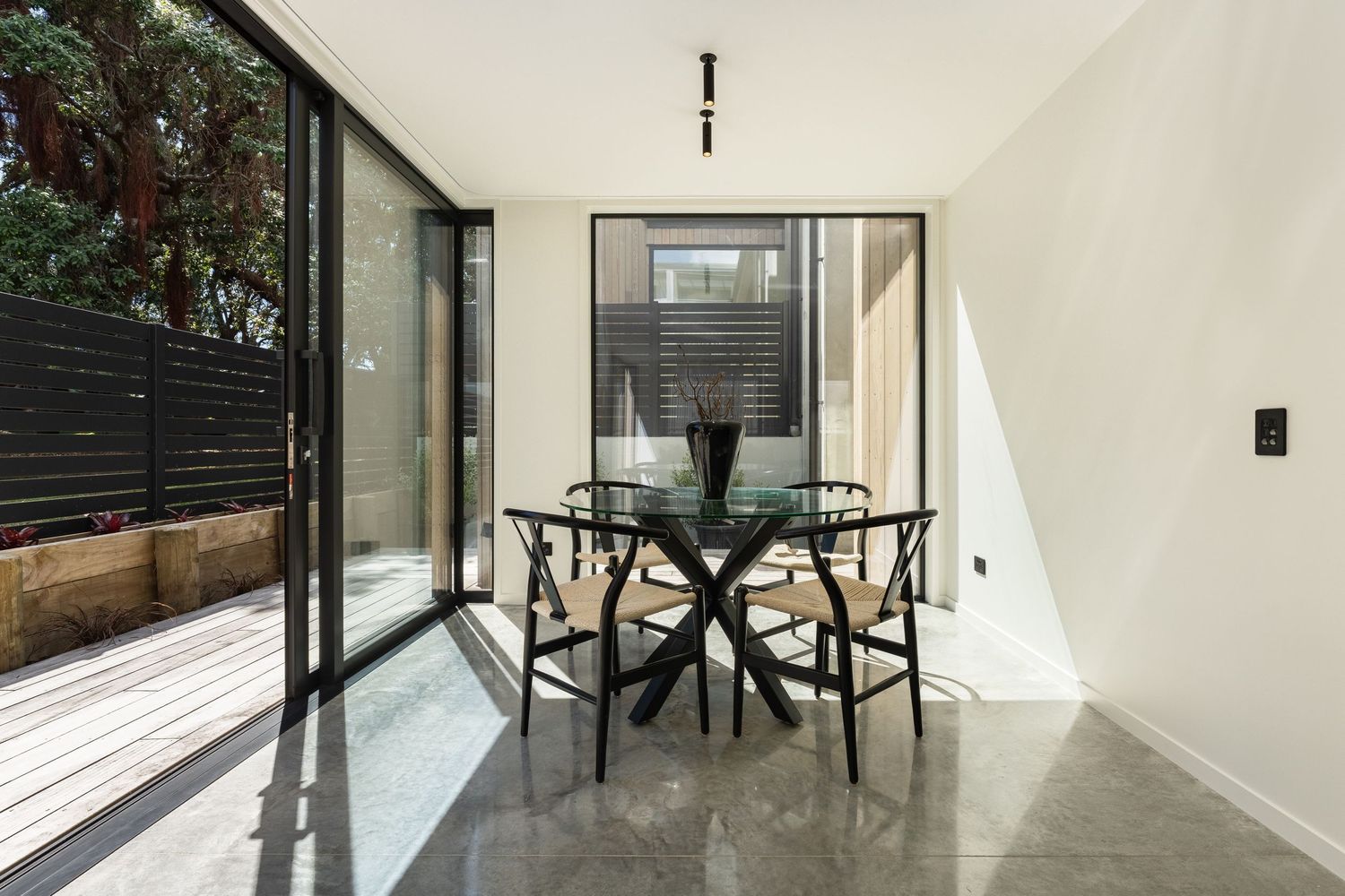 Modern dining area with round black table and chairs next to floor-to-ceiling windows in bright minimalist interior.