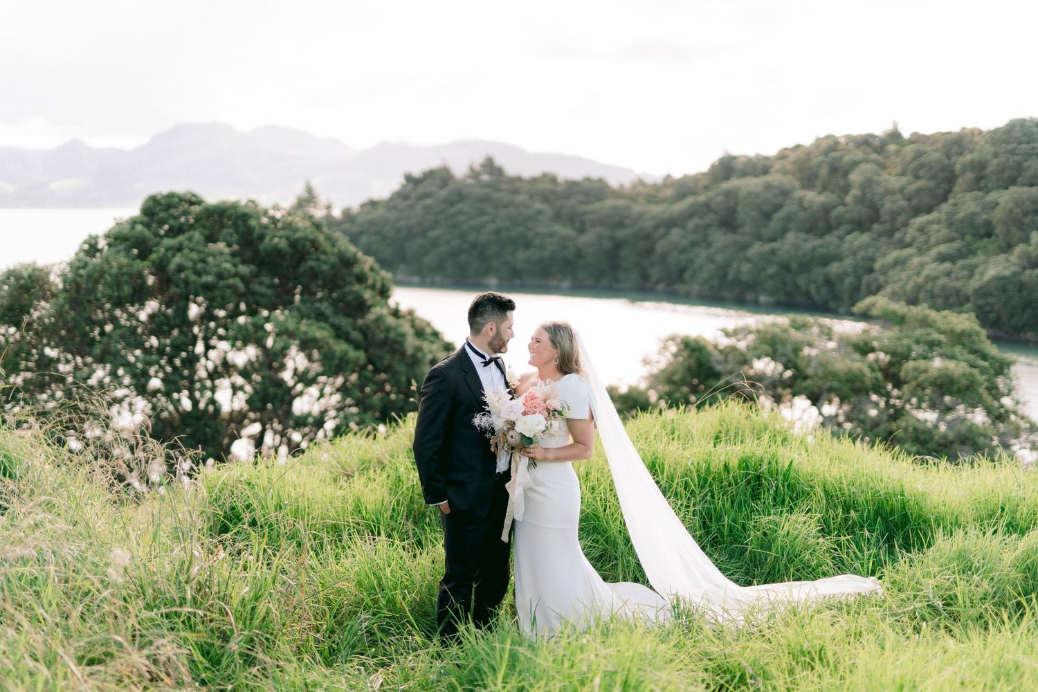 Couple poses together on a grassy hillside with scenic mountain views.
